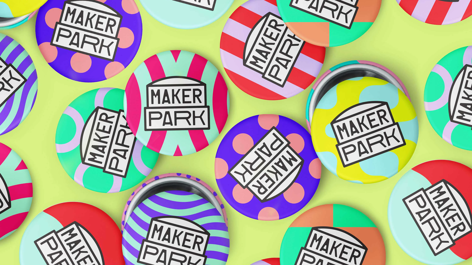 An assortment of button wins with various brightly colored graphics and the Maker Park logo are scattered in various arrangements on a green/yellow surface
