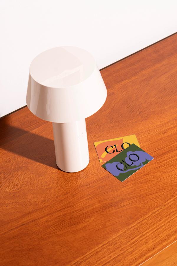 A white lamp and two colorful business cards with the word "CLO" on them sit on a wooden table