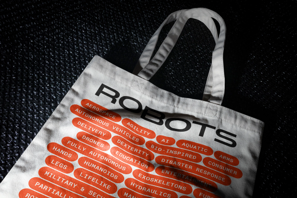 A tote bag with a grid of robot features and category tags, with the ROBOTS logo across the top
