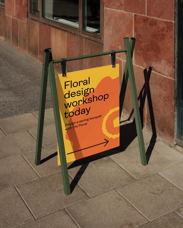 A-frame sidewalk sign with a poster reading "Floral design workshop today. Design a spring bouquet with Clo Floral," and an arrow pointing right.