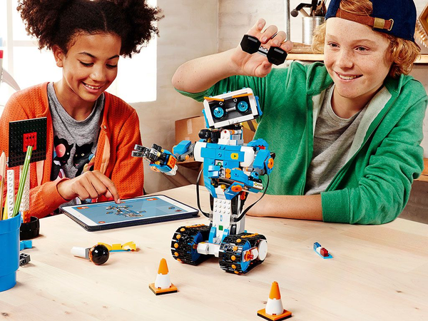 Two preteen children are shown building a LEGO robot and controlling it with an iPad